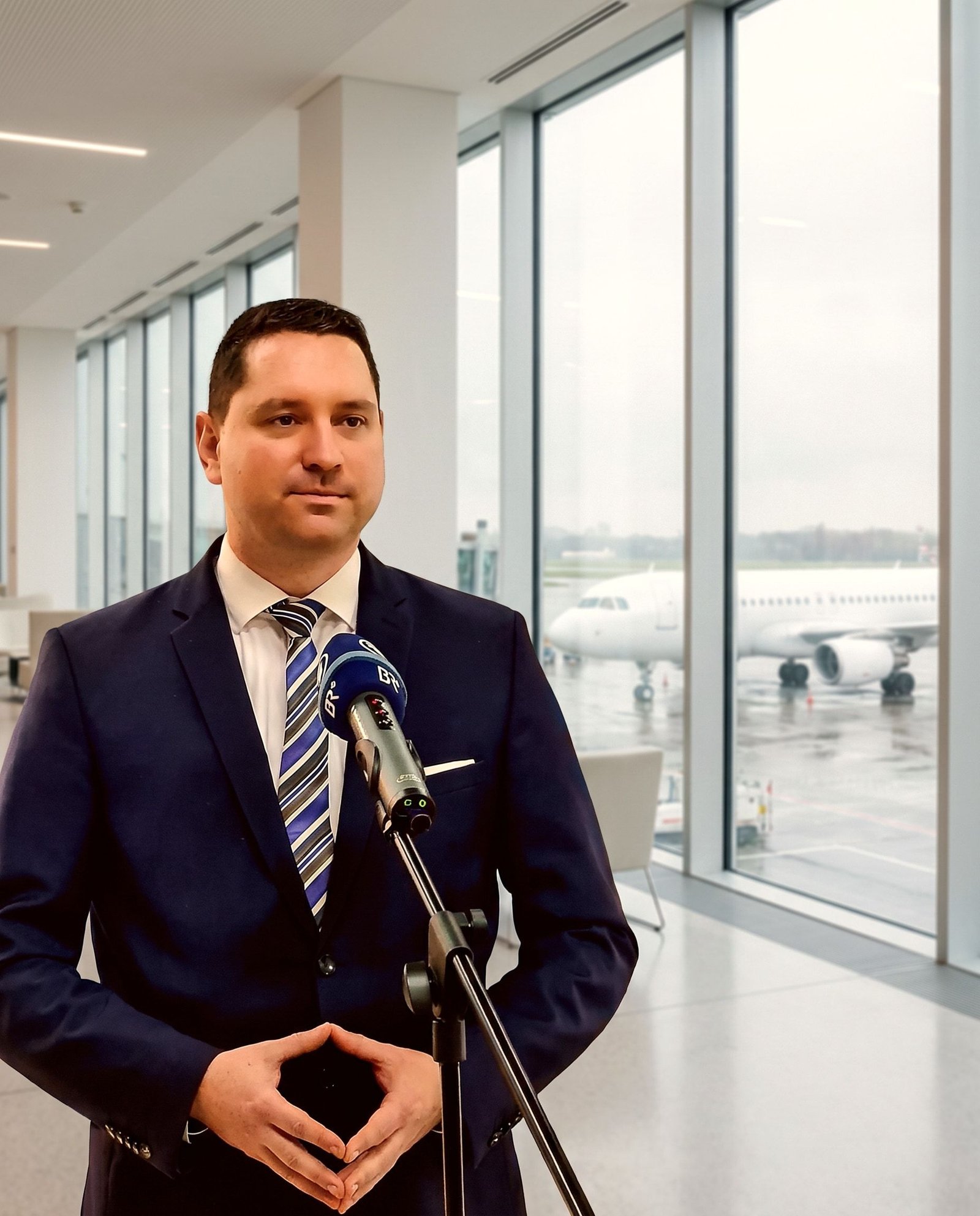 Roger Hohl giving an interview at an ARD microphone in an airport terminal